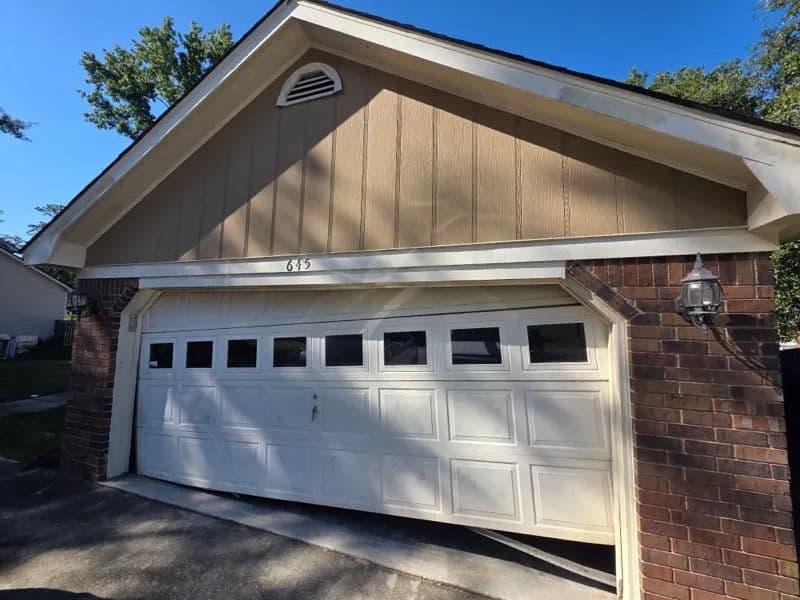 Residential garage with a white door and brick accents, featuring a clear blue sky above.
